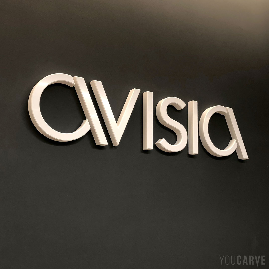 Réalisé par Avisia (technologies digitales) : logo mural en relief, découpe sur-mesure en PVC expansé blanc épaisseur 30 mm avec chanfreins, fixation mousse-double-face avec gabarit de positionnement.