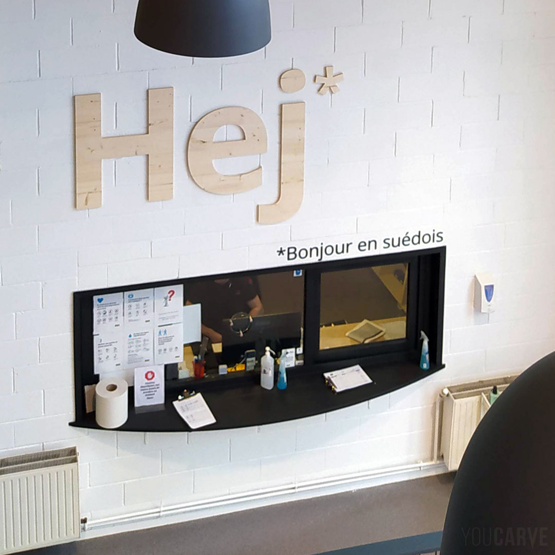 Réalisé par Ikea à Lomme : signalétique intérieure d’accueil « Hej » (Bonjour), lettres murales découpées en bois (épicéa épaisseur 19 mm) , fixation mousse-double-face avec gabarit de positionnement.