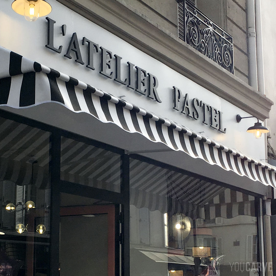 Réalisé par L'Atelier Pastel : enseigne boutique de décoration à Levallois Perret, lettres découpées en PVC expansé noir épaisseur 19 mm, fixation sur entretoises avec gabarit de perçage