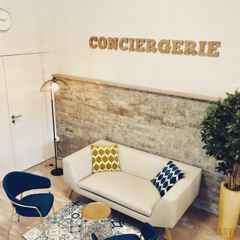 Réalisé par Toit et Moi, agencement d'espaces professionnels à Paris, signalétique d’un espace conciergerie réalisée avec des lettres découpées en bois (chêne épaisseur 19 mm), fixation mousse-double-face avec gabarit de positionnement.