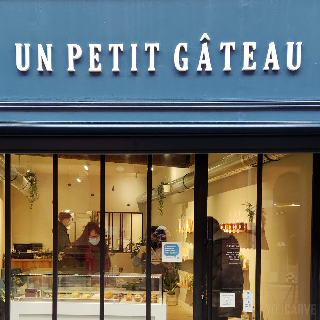 Réalisé par Un petit gâteau : enseigne pâtisserie à Toulouse, lettres en relief découpées en PVC expansé blanc épaisseur 19 mm, fixation mousse-double-face avec gabarit de positionnement.