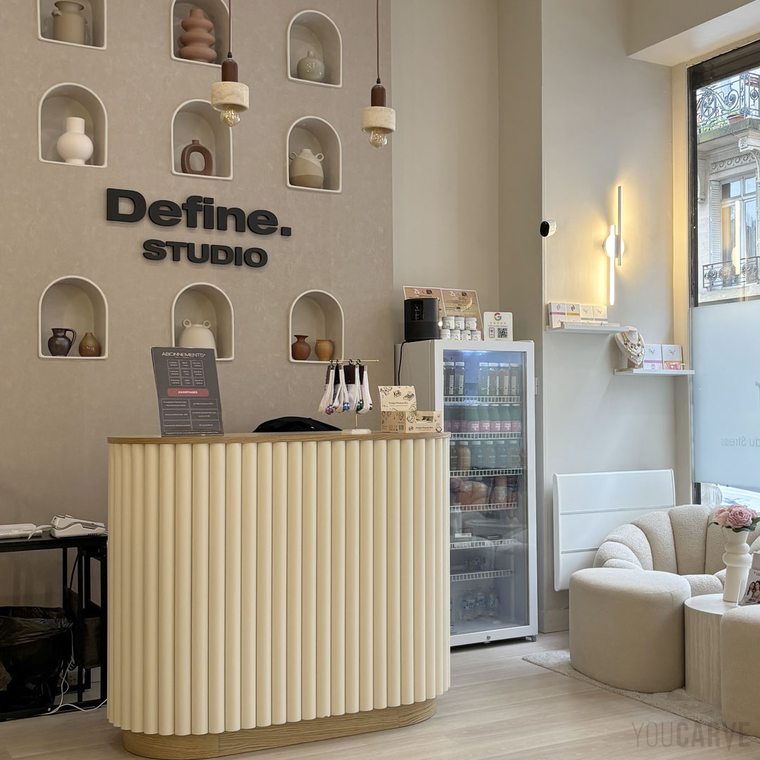 Define. Studio Paris - Logo mural en relief (PVC expansé noir ép. 19 mm) Enseigne murale intérieure "Define. Studio" à l’accueil, lettres découpées en PVC expansé noir, fixation mousse double-face sur un mur beige avec des niches décorées.