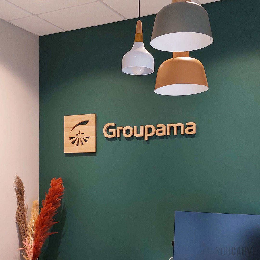 Logo mural pour Groupama Pays d’Oc en bois (chêne lamellé-collé, fixation mousse double-face) Logo mural Groupama découpé en bois (chêne lamellé-collé ép. 19 mm), fixé sur un mur de bureau de couleur vert forêt