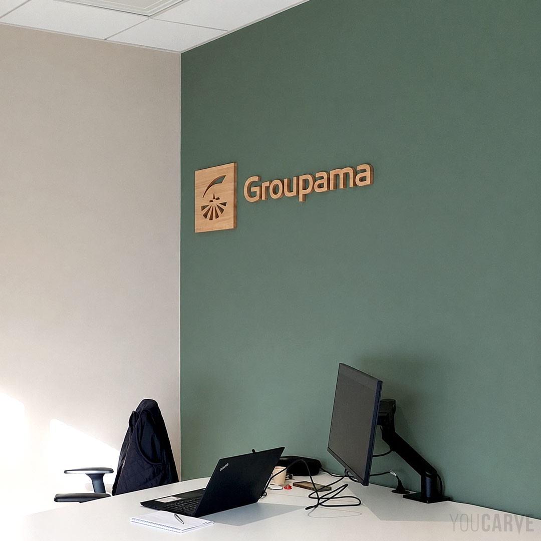 Logo mural pour Groupama Pays d’Oc en bois (chêne lamellé-collé, fixation mousse double-face) Logo mural Groupama découpé en bois (chêne lamellé-collé ép. 19 mm), fixé sur un mur de bureau de couleur vert sauge