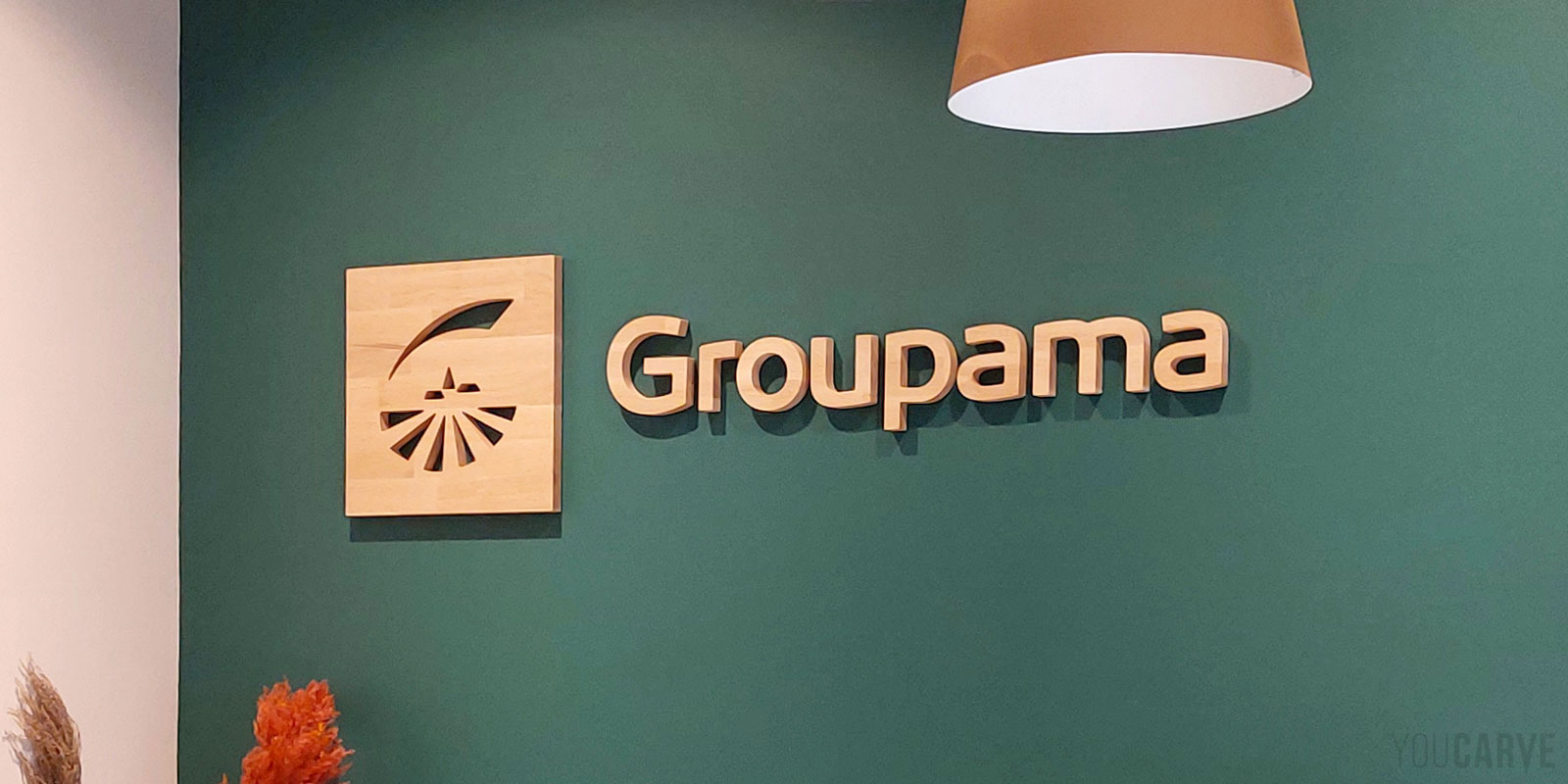 Exemple de logo mural déployé au niveau régional pour le réseau d’agences Groupama Pays d’Oc Logo mural Groupama découpé en bois (chêne lamellé-collé ép. 19 mm), fixé sur un mur de bureau de couleur vert forêt